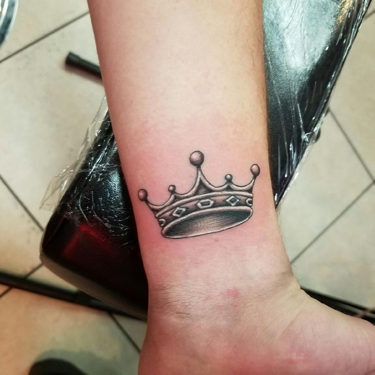 a black and white photo of a crown tattoo on the arm with stars around it