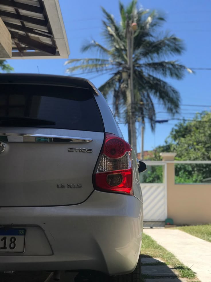 the back end of a white car parked in front of a house with palm trees