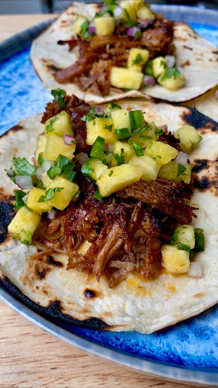 two tacos with meat, pineapple and onions on a blue plate sitting on a wooden table