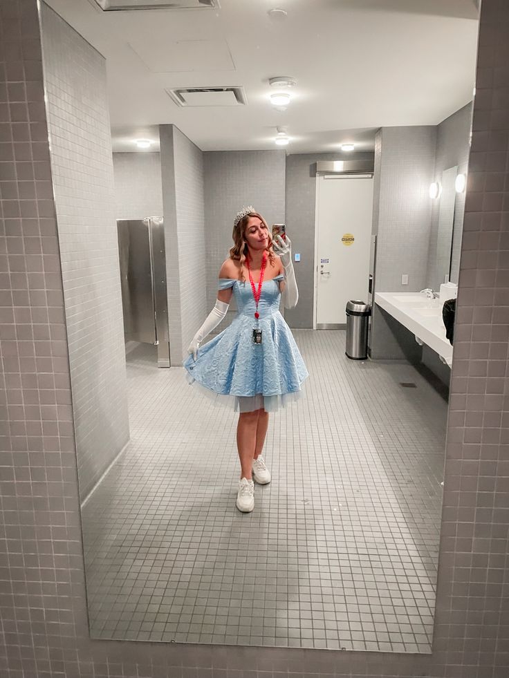 a woman in a blue dress taking a selfie with her cell phone while standing in a bathroom