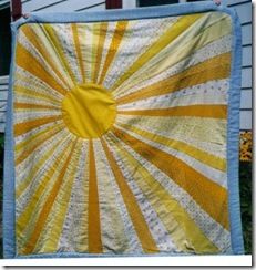 a large yellow and white quilt hanging from the side of a house with sunbursts on it