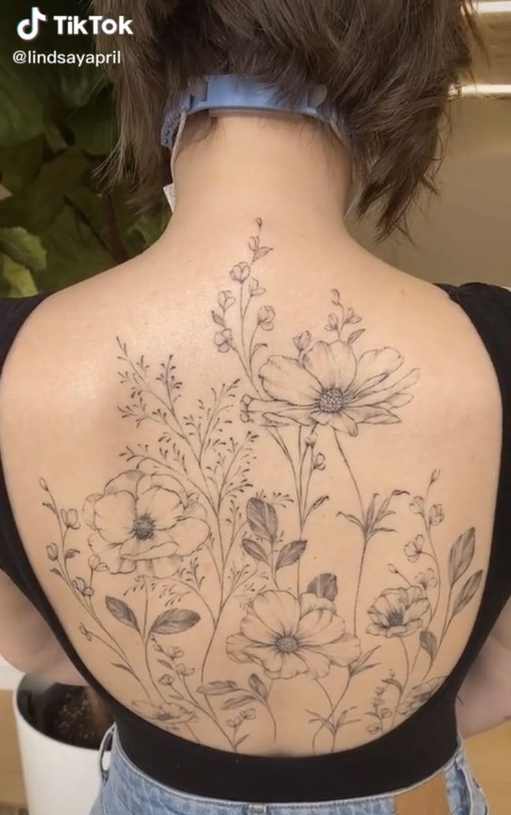 the back of a woman's shoulder with flowers and leaves tattooed on her body