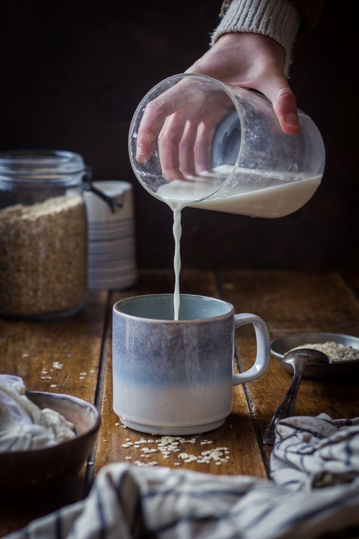 someone pouring milk into a cup on top of a wooden table