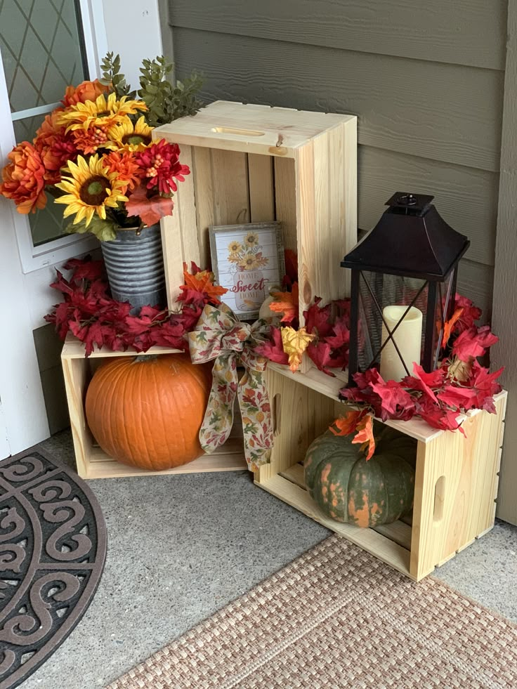 a wooden crate filled with pumpkins and fall leaves sitting on the front porch next to a lantern