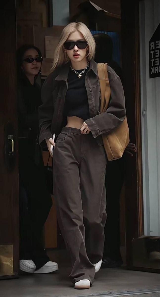 a woman in black top and brown pants walking out of a building with her hand on her hip