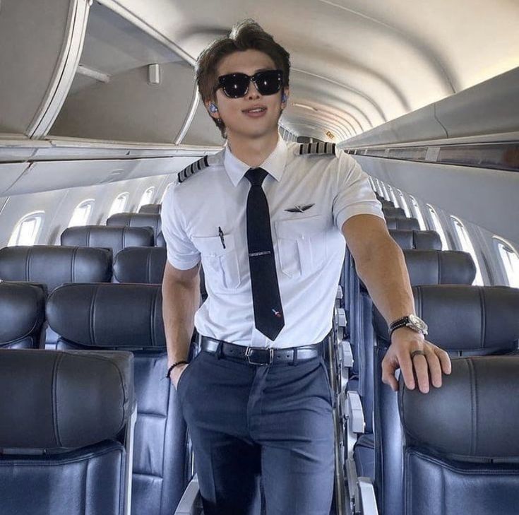 a man wearing sunglasses and a tie standing in the aisle of an airplane with his hands on his hips