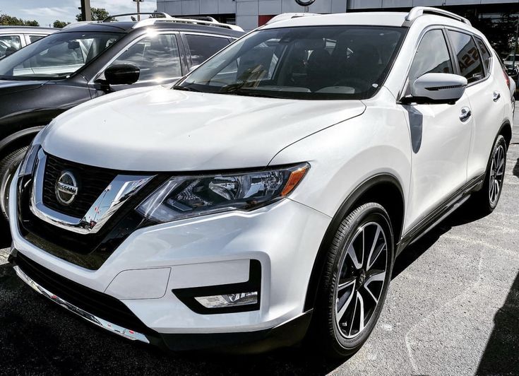 the front end of a white nissan suv parked in a parking lot next to other cars