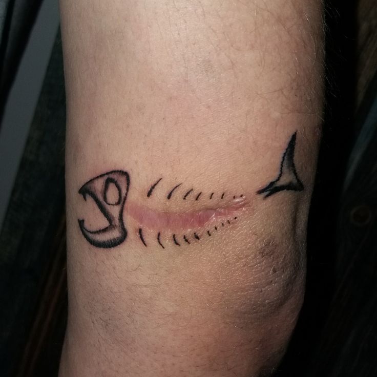 a small tattoo on the leg of a man with an arrow and fishbones