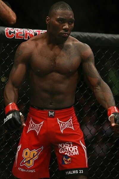 a man in red shorts standing next to a fence