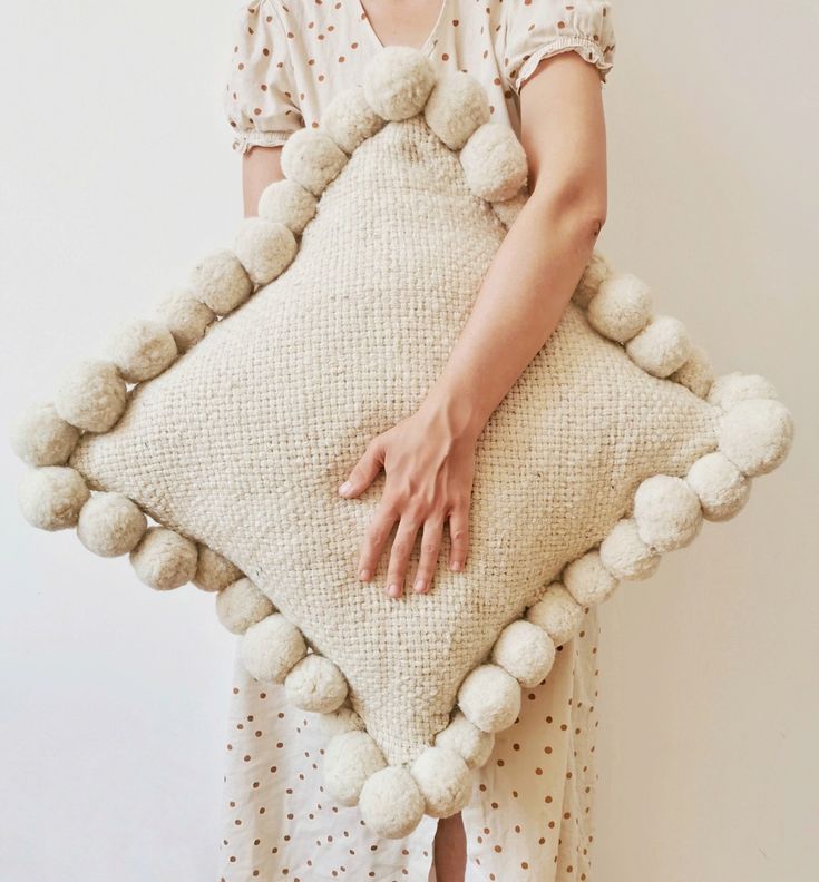 a woman holding a pillow with pom poms on it