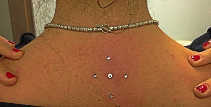 the back of a woman's neck with red nail polish on her nails and jewelry