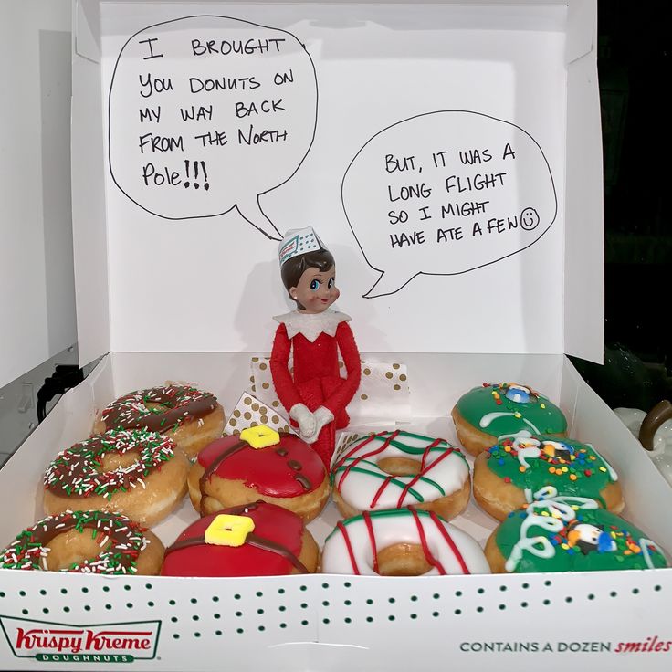 an elf is sitting in a box filled with doughnuts that have been decorated