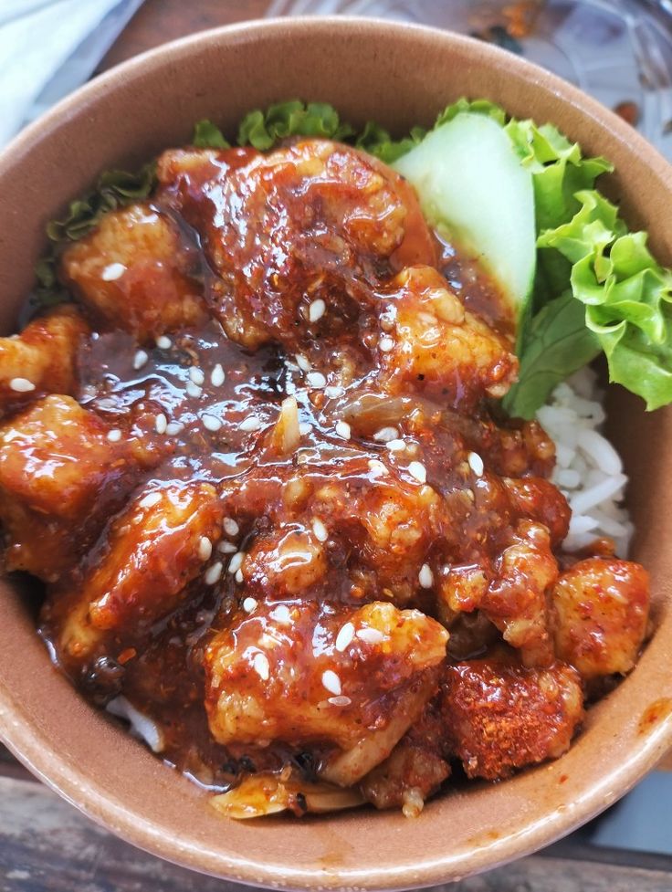 a brown bowl filled with meat and rice next to lettuce on top of a wooden table