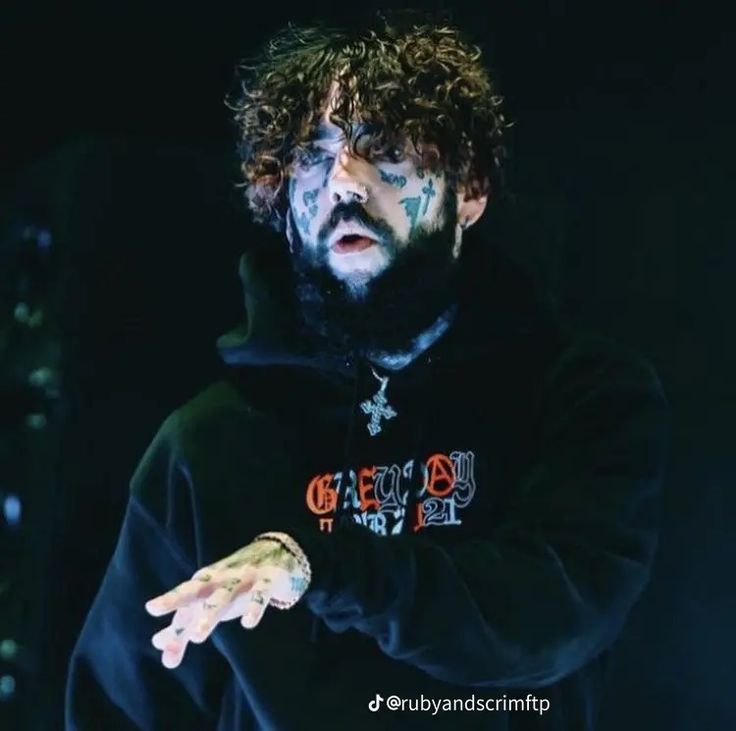 a bearded man in a black hoodie holding his hands out to the side while standing on stage