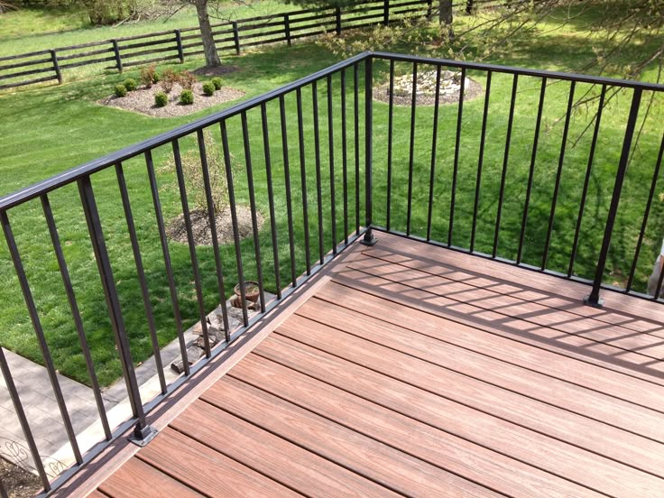 a wooden deck with black iron railings and green grass in the backround