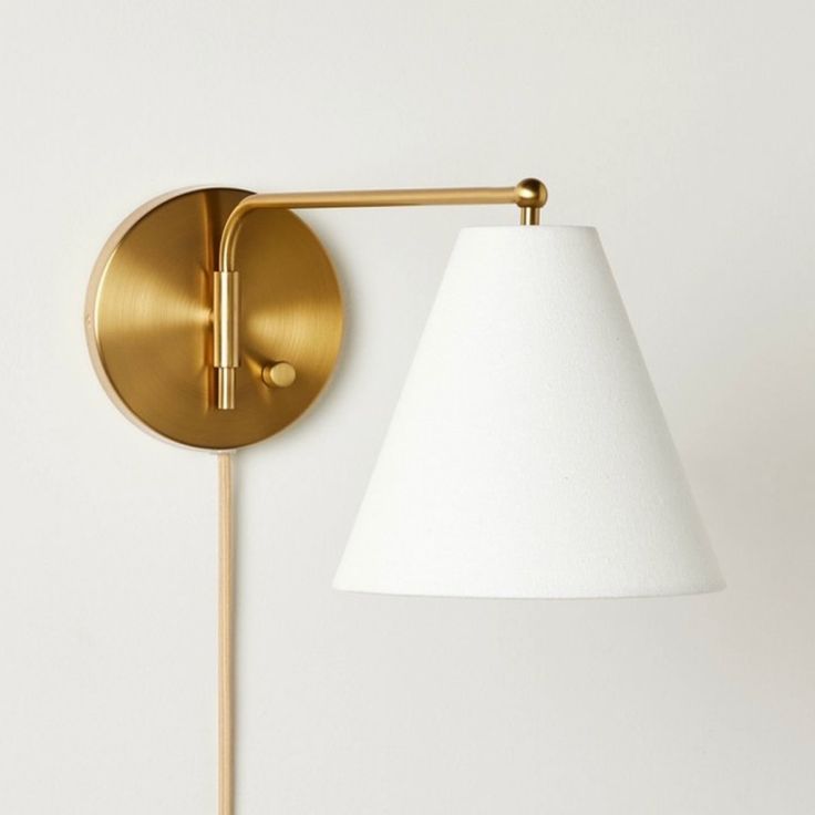 a gold wall light with a white shade on the side and a wooden stick next to it