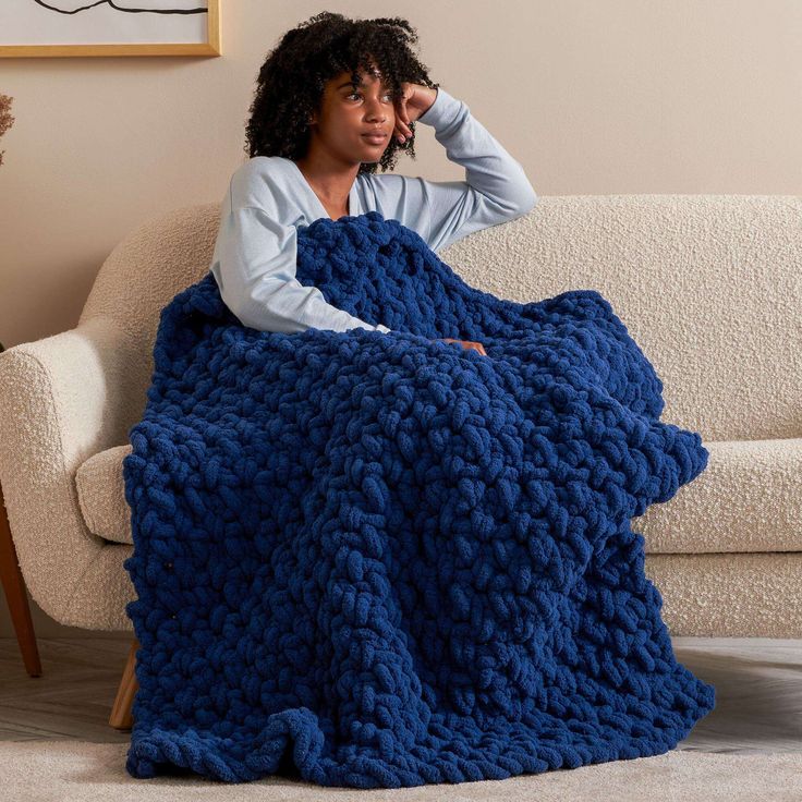 a woman is sitting on a couch wrapped in a blue crochet afghan blanket