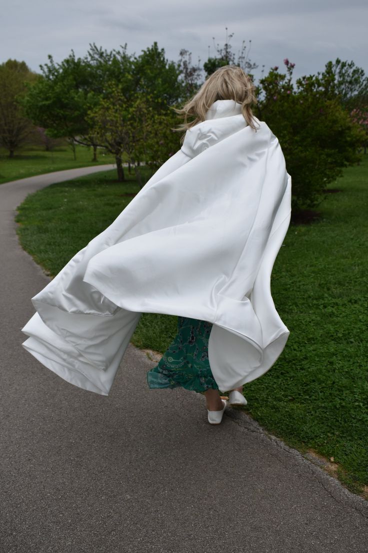 a woman is walking down the road in a white coat