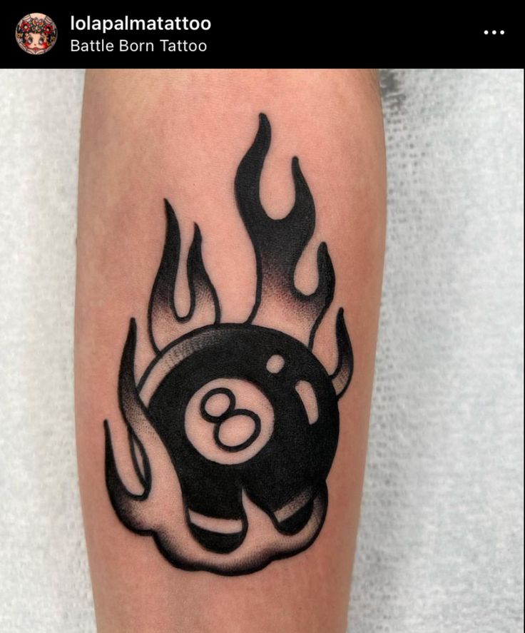 a black and white photo of a tattoo with flames on the leg, which has an eight ball in it