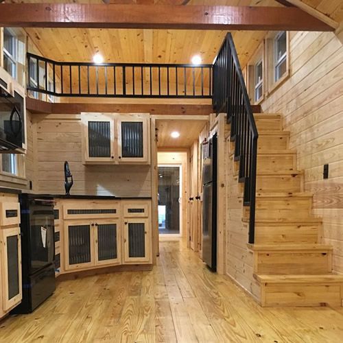 the interior of a tiny house with wood flooring and stairs leading up to an upper level kitchen