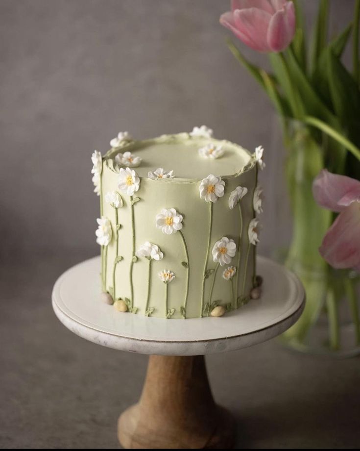 a green cake sitting on top of a white plate next to pink tulips