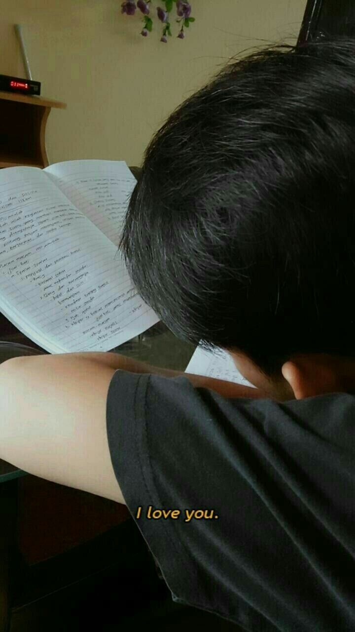 a boy is reading a book while sitting at a desk with an open book on it