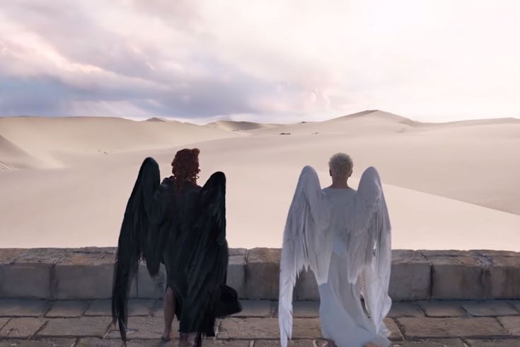 two people dressed in white and black with wings on their backs walking down a stone walkway