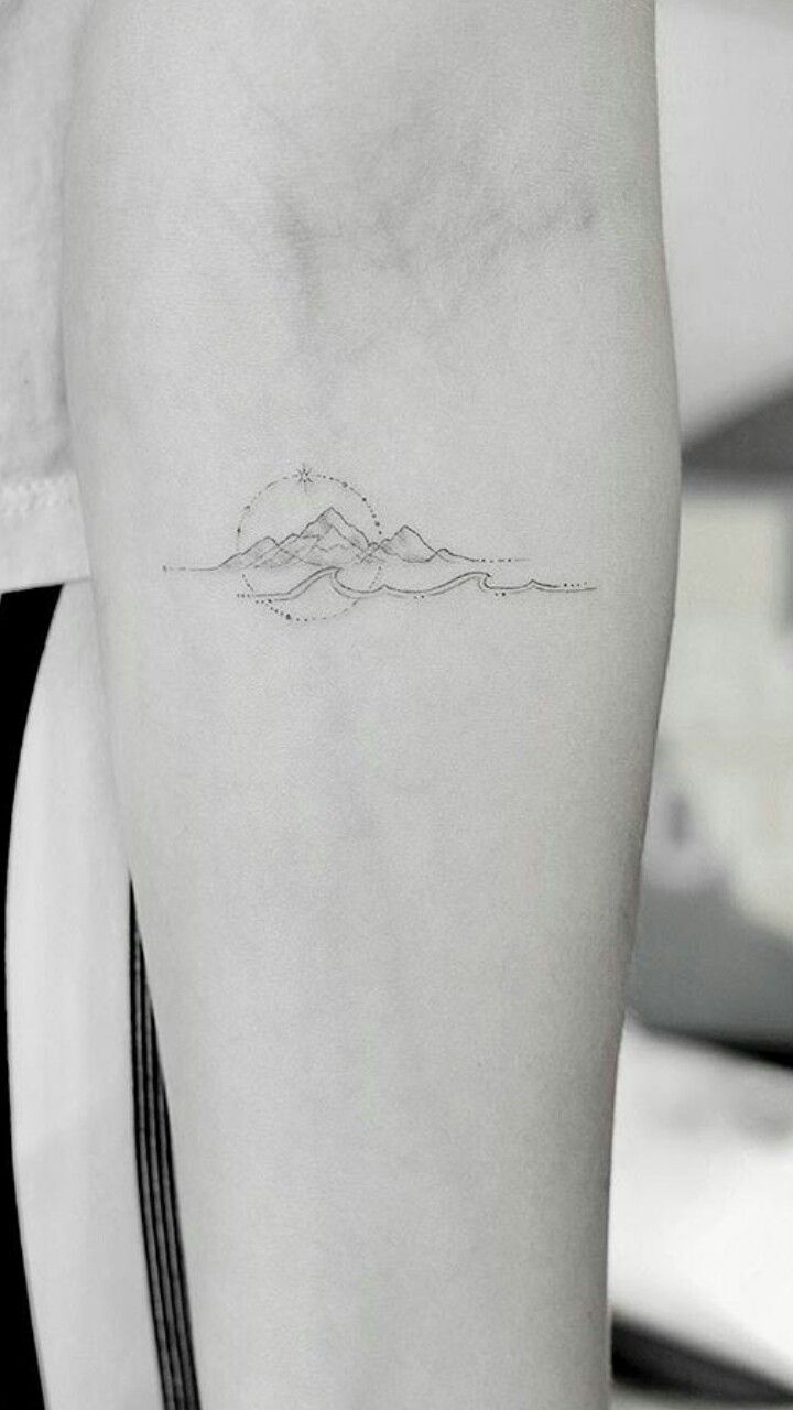 a person with a small mountain tattoo on their left arm and the outline of a mountain behind them