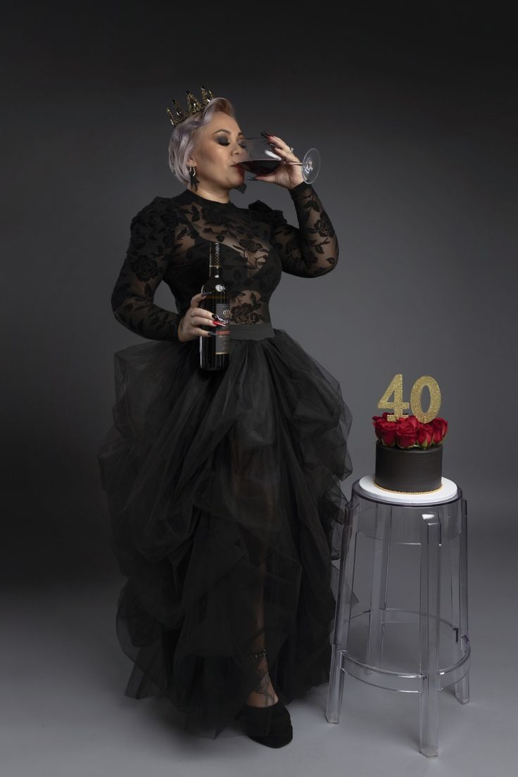 a woman in a black dress standing next to a cake with the number 40 on it