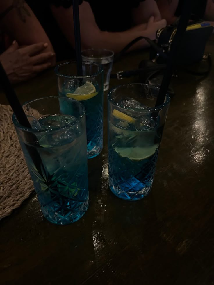 three glasses filled with blue liquid on top of a wooden table next to each other