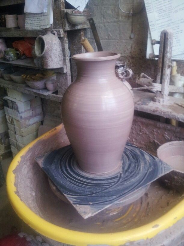 a large vase sitting on top of a yellow bowl in a pottery shop filled with pots