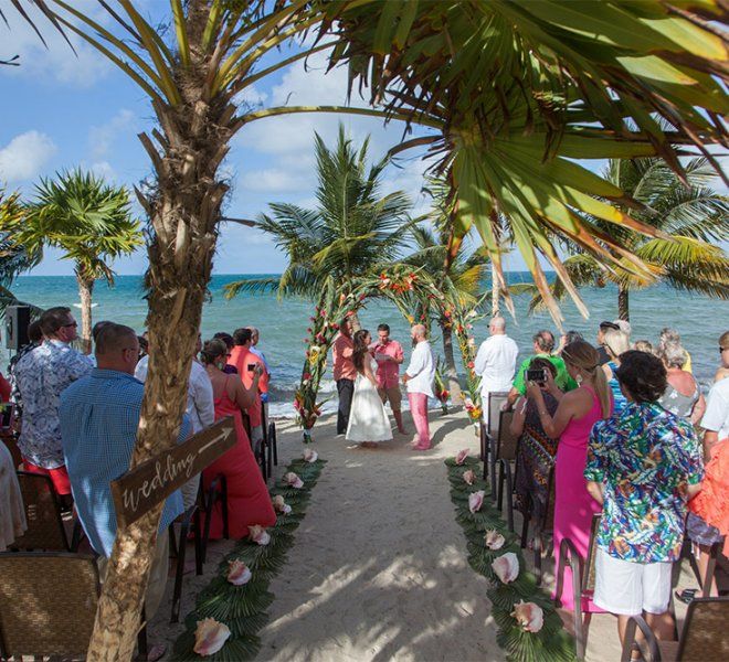 a wedding ceremony on the beach with palm trees and people walking down the aisle to the water