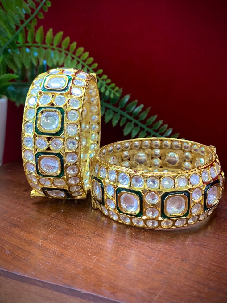 Experience the luxury of these Emani kundan bangle bracelets. Each piece comes as a pair and features emerald green meenakari work, a premium gold plating, and a screw open closure for easy use. With a width of about 1.25 inches, these exquisite bangle bracelets make the perfect accessory for any occasion. Bollywood Style Kundan Hand-set Bracelets, Bollywood Style Hand Set Kundan Bracelets, Ceremonial Green Bracelets With Tilla Detail, Festive Kundan Bangle Bracelets, Gold Plated Meenakari Bangle Bollywood Style, Gold Plated Meenakari Chandbali Bracelets, Kundan Chandbali Bracelet As Gift, Kundan Chandbali Bracelets For Gifts, Kundan Cutdana Bangle Bracelets