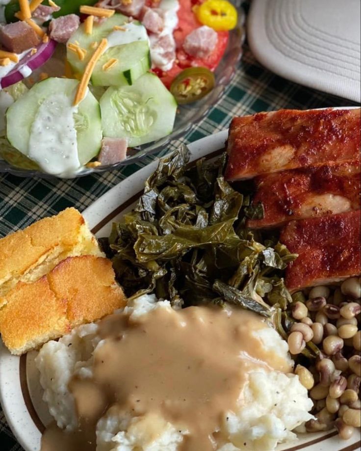 a white plate topped with meat, mashed potatoes and vegetables next to a bowl of salad