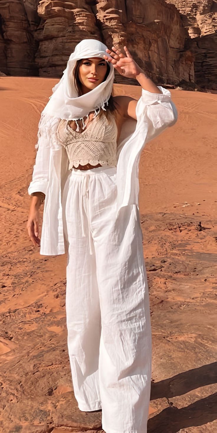 a woman standing in the desert with her hands on her head and wearing a white outfit