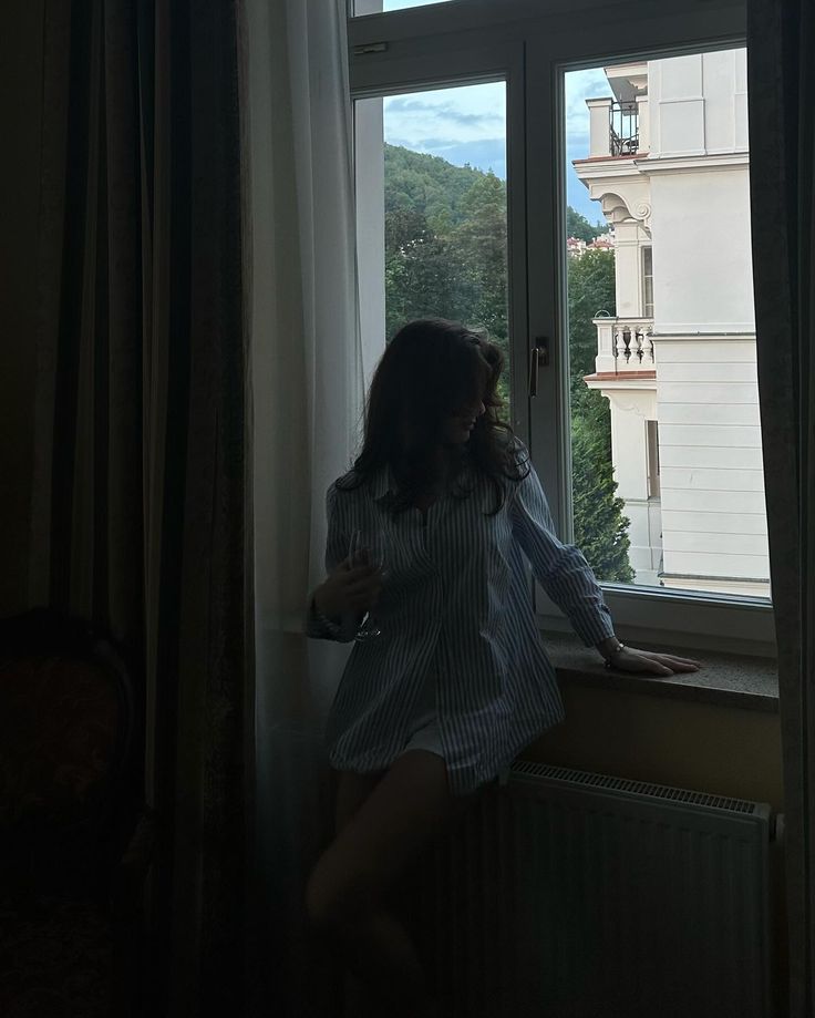 a woman standing in front of a window looking out