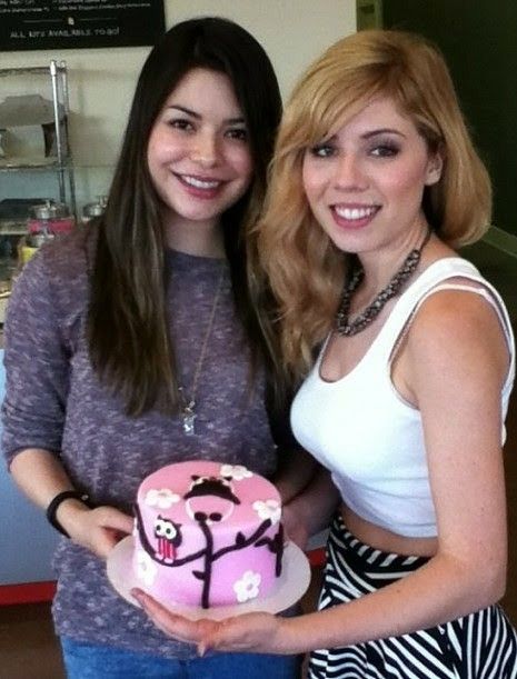 two women standing next to each other holding a pink frosted cake with the word hello kitty on it