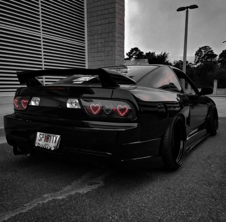 the rear end of a black sports car parked in front of a tall brick building