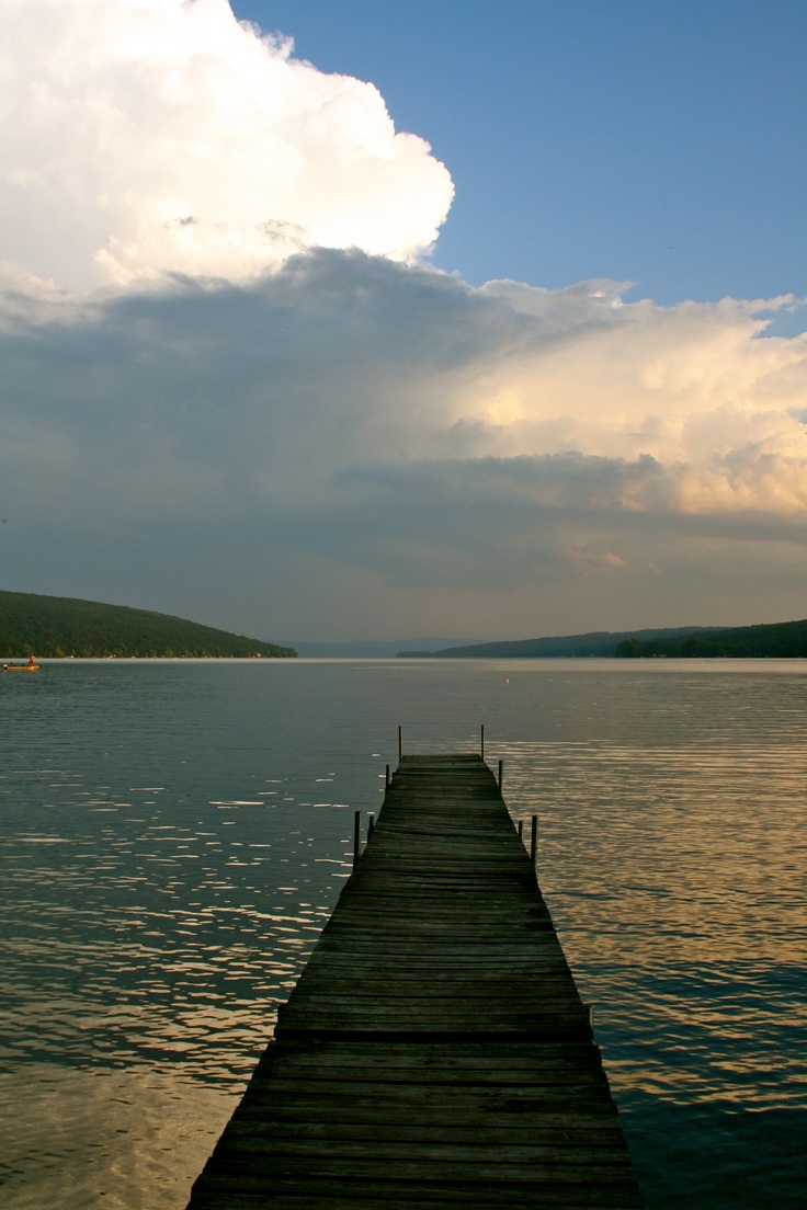 a long dock extending out into the water under a cloudy sky with boats in the distance