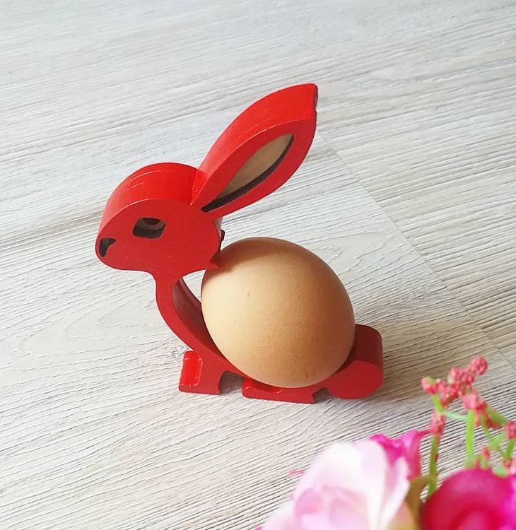 an egg in the shape of a rabbit sitting next to a pink flower on a table