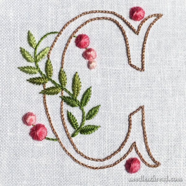 the letter q is made up of flowers and leaves on a white linen background with stitching