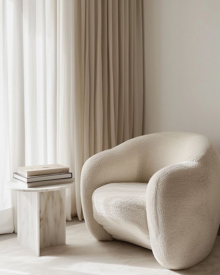 a white chair sitting in front of a window next to a table with a book on it