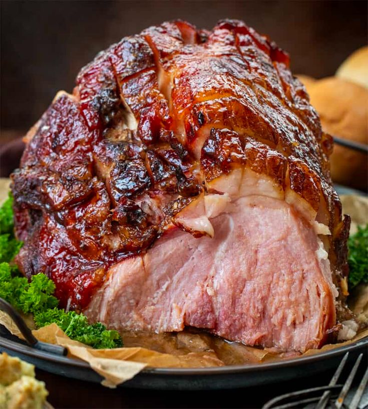 a large ham is on a plate with some bread and other food items around it