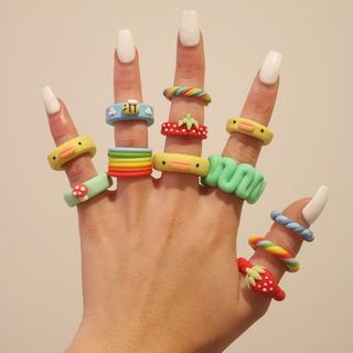 a woman's hand with several rings on it, all decorated in different colors