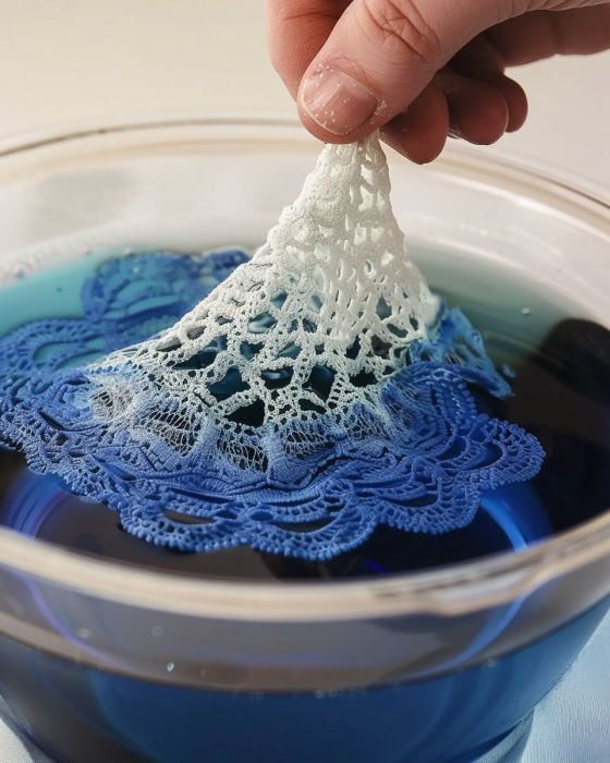 a hand is holding a white doily over a blue liquid in a glass bowl