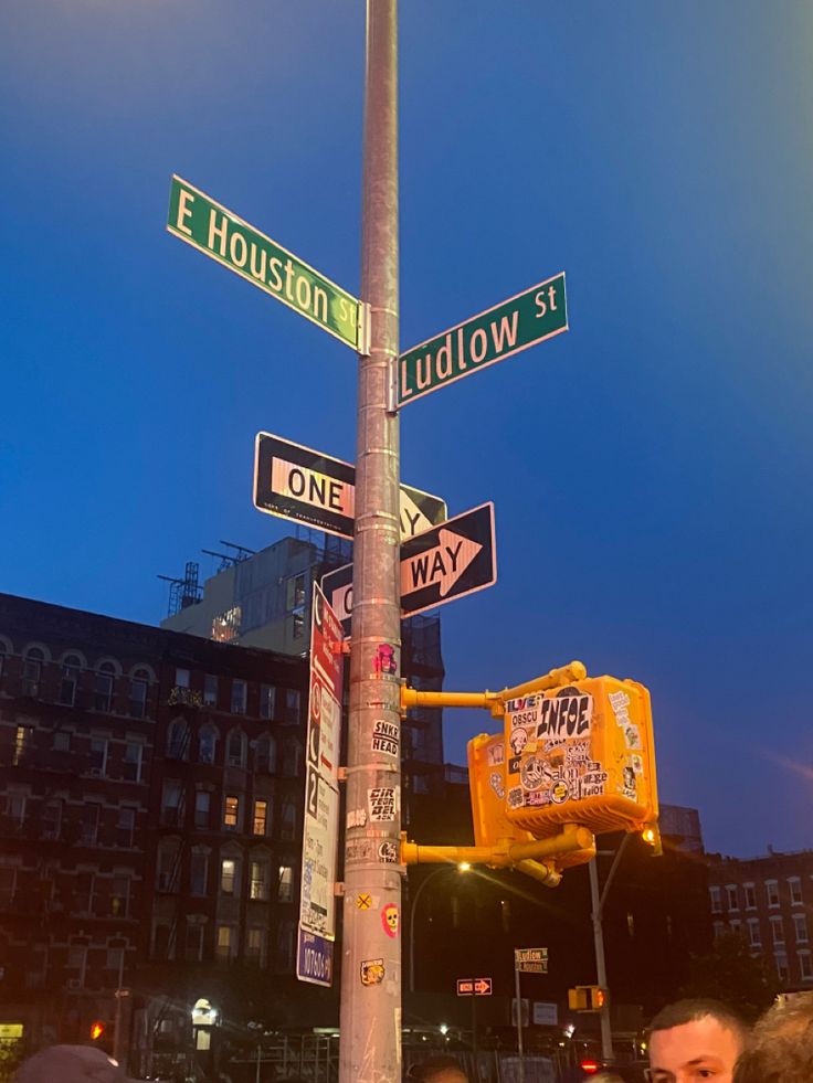 people are standing under street signs on a pole in front of some buildings at night