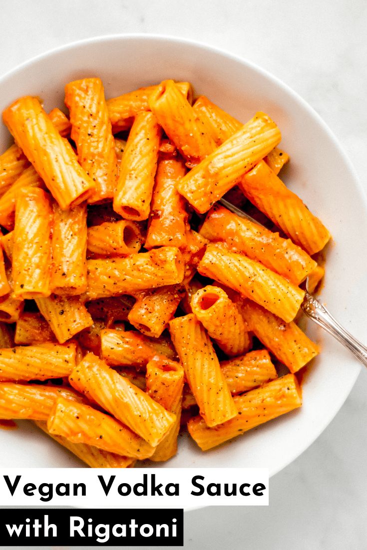 a white bowl filled with vegan vodka sauce covered in rigantii pasta next to a spoon