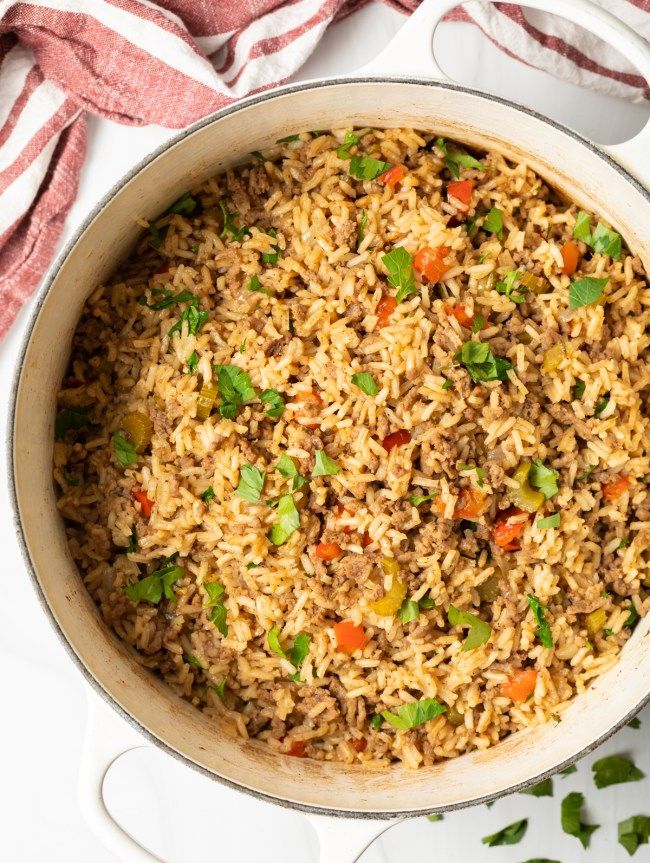 a pot filled with rice and vegetables on top of a white table cloth next to a red striped towel