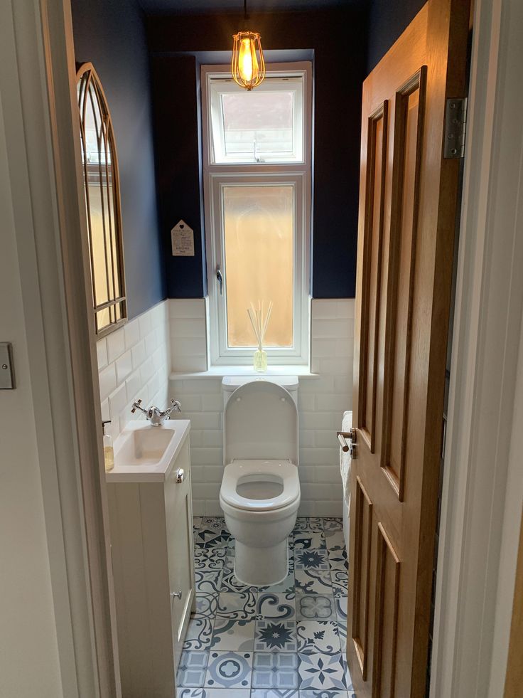 a white toilet sitting next to a sink in a bathroom under a window on top of a tiled floor