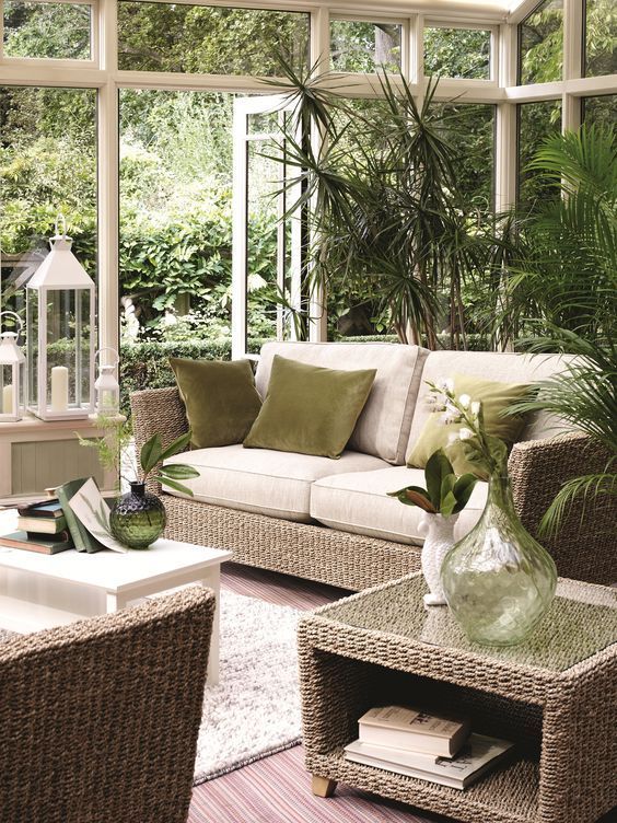 a living room with wicker furniture and plants in the window sill, surrounded by greenery